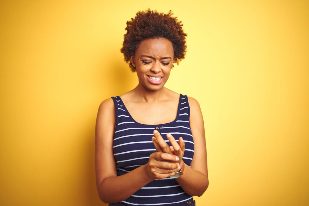 Beauitul african american woman wearing summer t-shirt over isolated yellow background Suffering pain on hands and fingers, arthritis inflammation